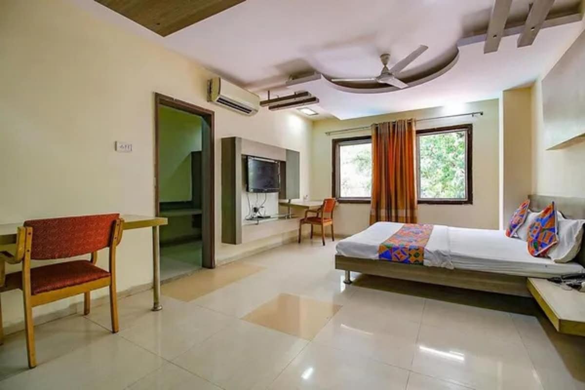 A hotel room with a bed, a desk, a chair, a television, and a window with curtains.