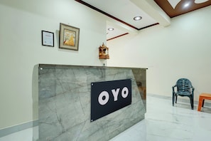 Una recepción con un letrero que dice 'OYO' en el vestíbulo de un hotel con piso de mármol e iluminación empotrada en el techo.