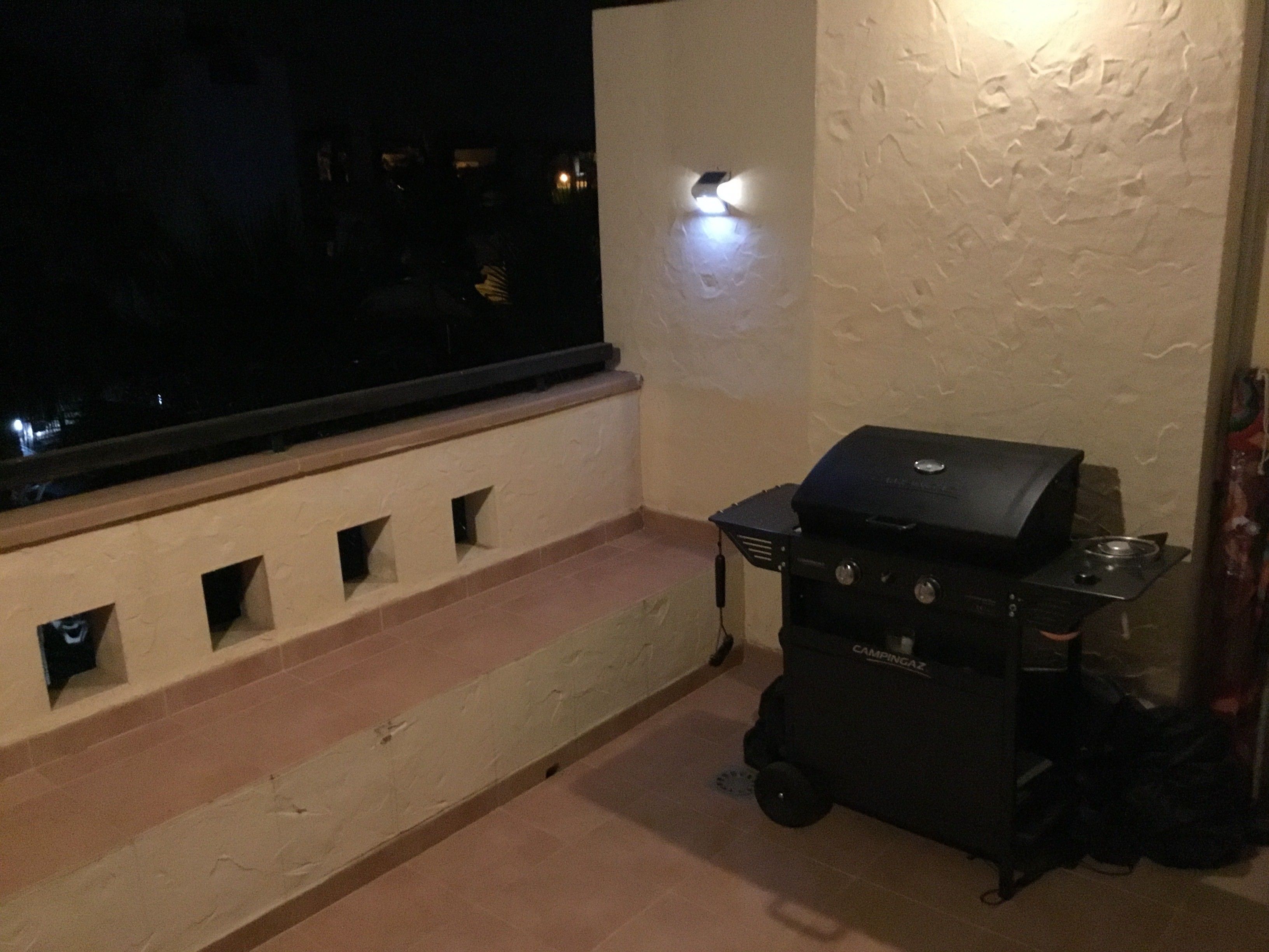 A balcony with a grill and a window overlooking a dark exterior.
