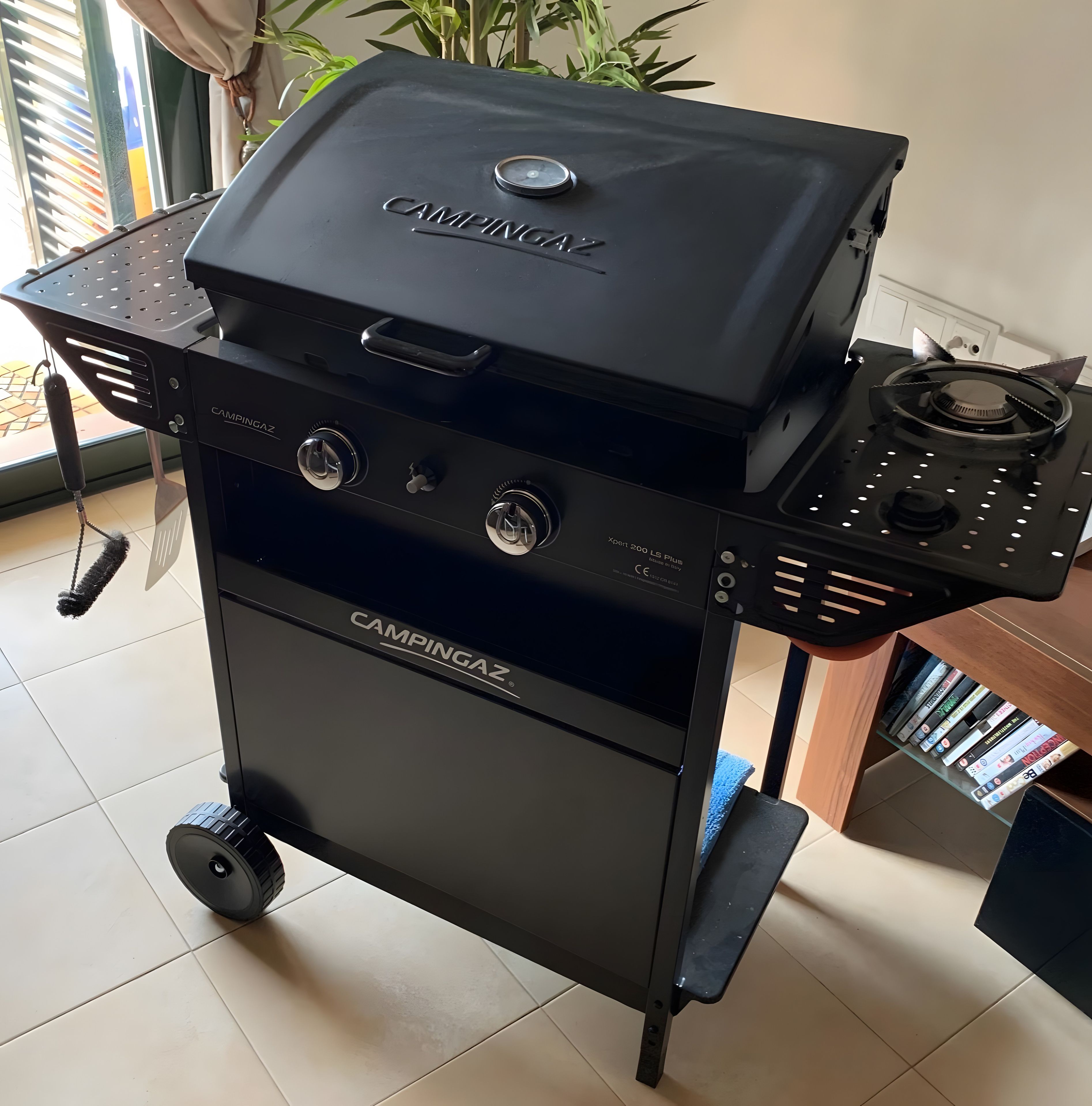 A black camping gas barbecue with wheels, a control panel, and a gas stove.
