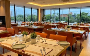 A restaurant with multiple tables, each set with plates, cutlery, and glasses. - Samasth Legacy  (Mysore)