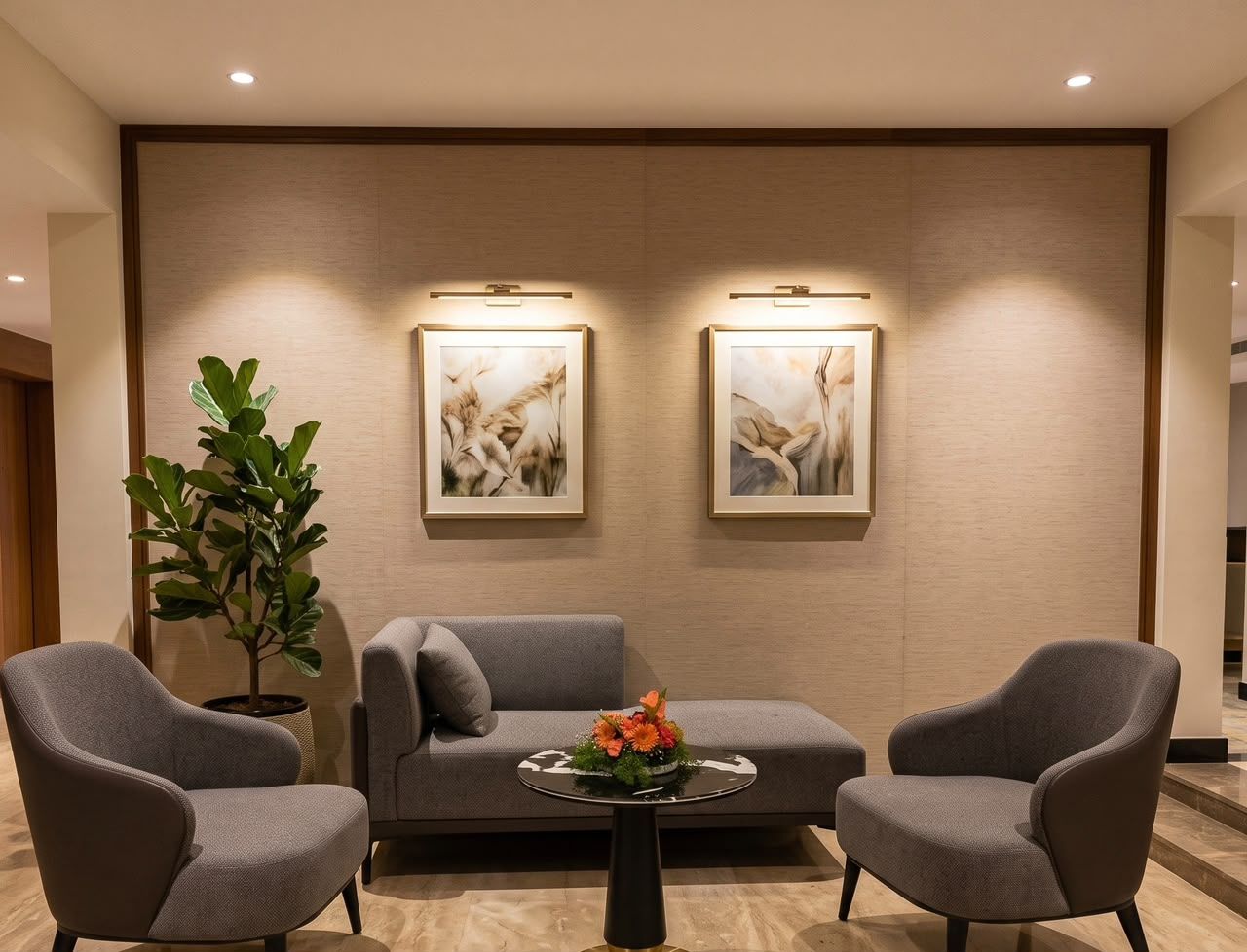 Un área de descanso moderna con un sofá, dos sillones, una mesa de centro con un centro de mesa floral y dos lámparas fijadas a la pared.