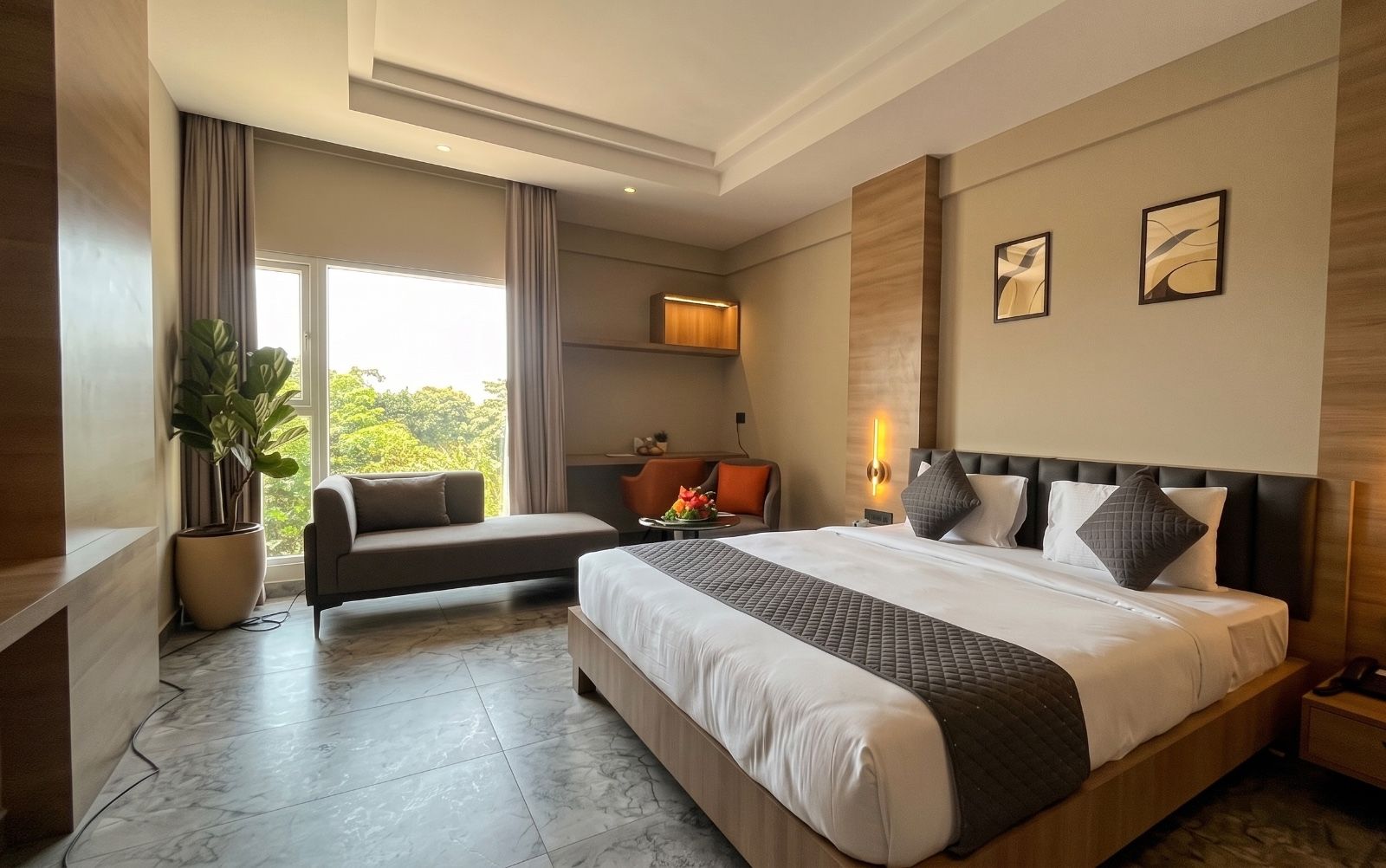 A modern hotel room with a large bed, a sofa, a desk, and a view of greenery outside.