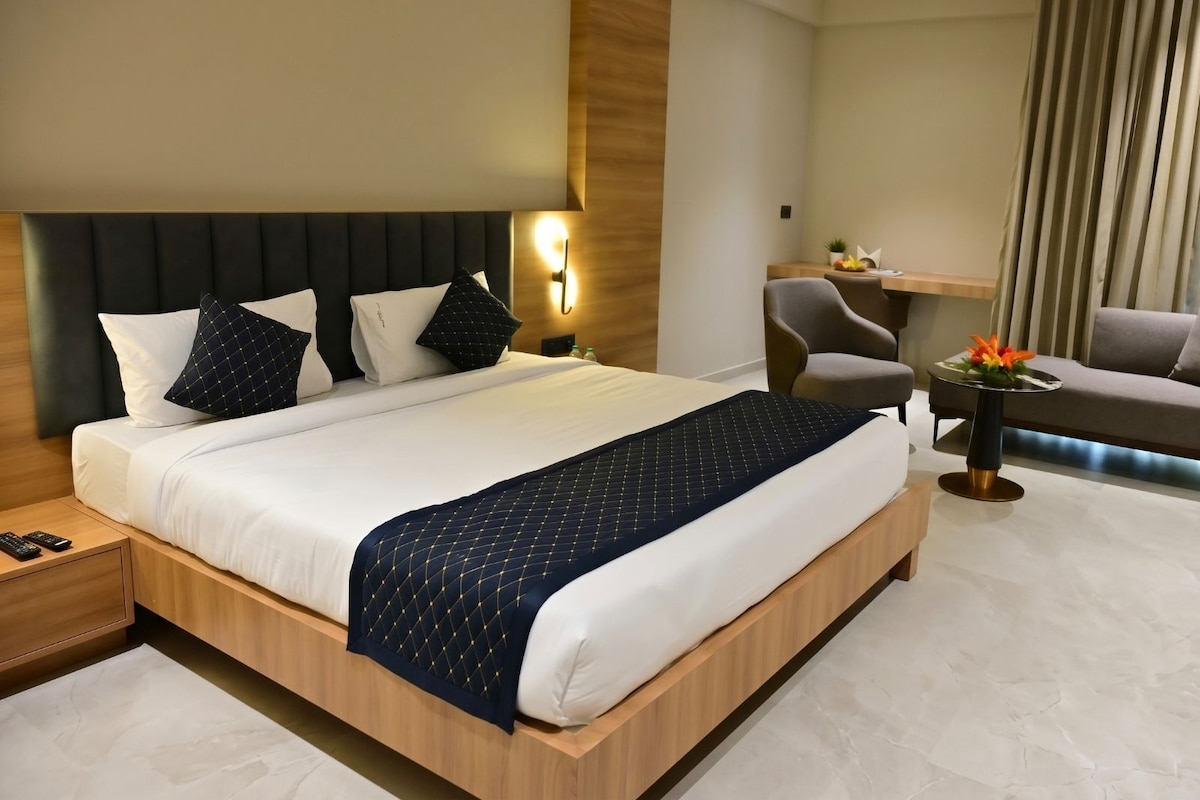 A hotel room with a large bed, a desk, a chair, and a small table with flowers.