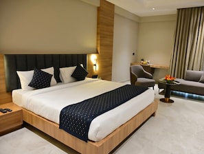 A hotel room with a large bed, a desk, a chair, and a small table with flowers. - Samasth Legacy  (Mysore)