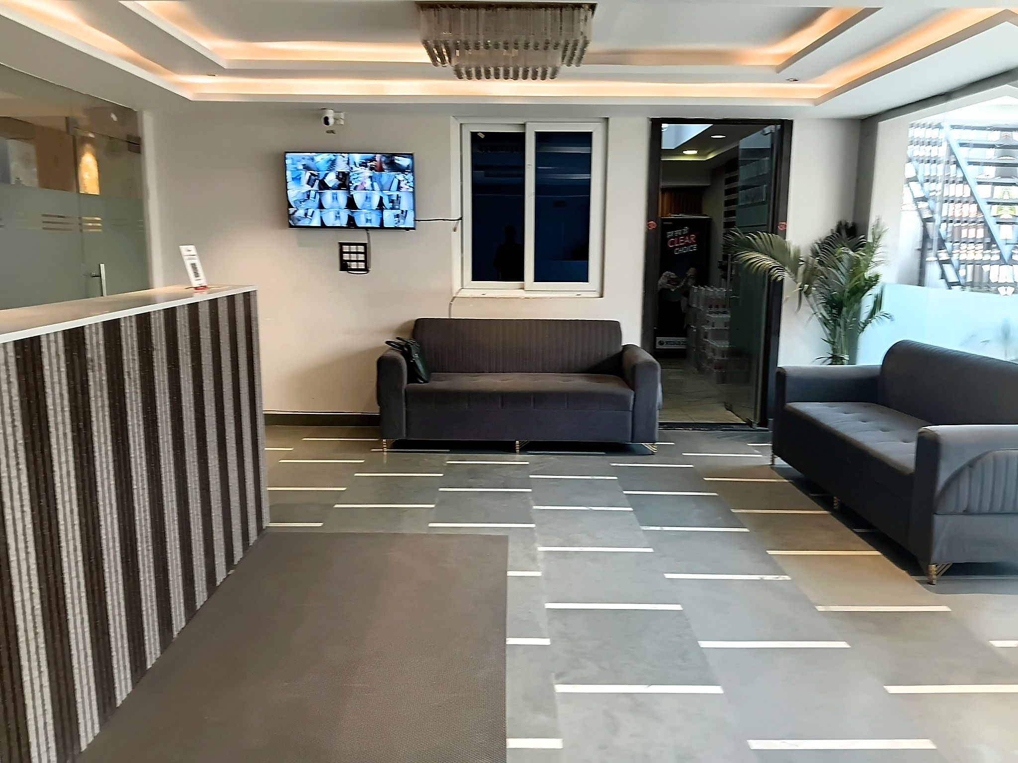 Un área de recepción con mostrador, una sala de estar con dos sofás, un televisor montado en la pared y un piso con diseño.