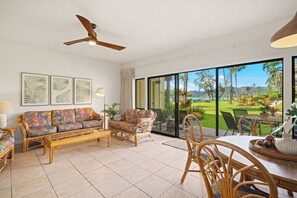 A spacious living room with a large sliding glass door leading to a tropical garden view. - Lae Nani 316, Ocean View, Tropical Oasis, Steps to Beach and Town (Kapaa)