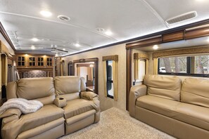 A well-lit RV interior with leather sofas, a kitchen area, and a large window. - Peaceful and cozy-1 bedroom RV in Lee, Fl on private river view lot (Lee)