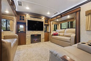 Ein gemütliches Wohnmobil-Interieur mit einem Flachbildfernseher, einem Kamin, Ledersofas und einer Wand mit Steinverkleidung.