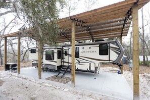 A covered RV park with a large RV named 'MONTANA' parked under a wooden pavilion. - Peaceful and cozy-1 bedroom RV in Lee, Fl on private river view lot (Lee)