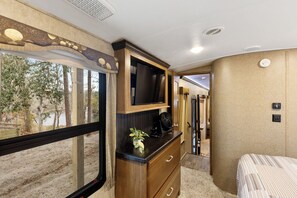 A compact RV interior with a bed, a kitchenette, a television, and a window offering a view of trees and a body of water. - Peaceful and cozy-1 bedroom RV in Lee, Fl on private river view lot (Lee)