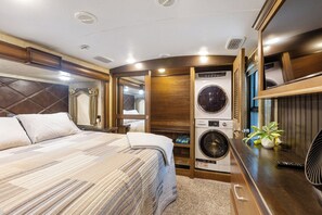 Ein kleiner, gut beleuchteter Raum mit einem Bett, einer Waschmaschine und einem Tisch mit einer Pflanze.