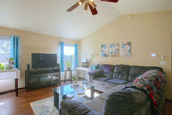 A living room with a flat-screen TV, a sofa, a coffee table, and a ceiling fan.