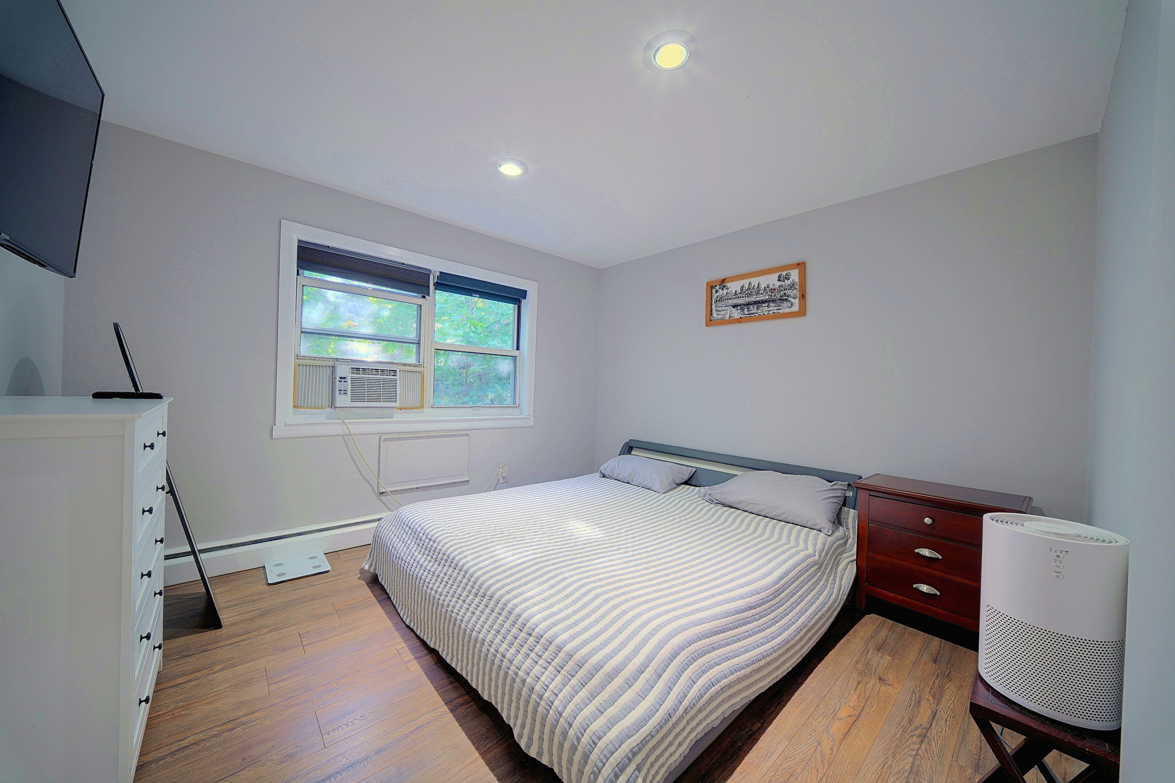 Un dormitorio con cama, cómoda, ventana y radiador.