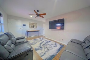 Una sala de estar con sofás de cuero, un televisor de pantalla plana, un ventilador de techo y una alfombra con diseño de mármol.