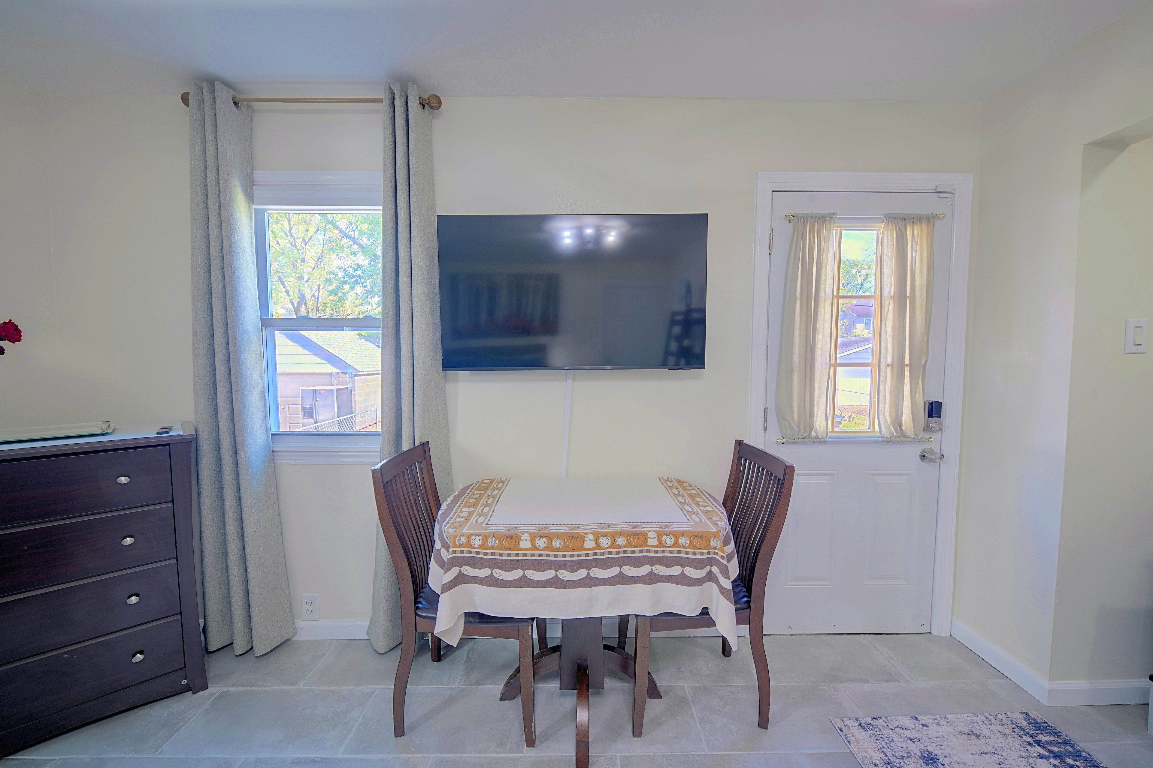 Een eetgedeelte met een tafel gedekt voor vier personen, een donker houten dressoir, een flatscreen televisie aan de muur en een deur met een raam.