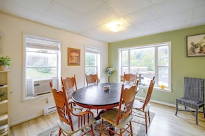 A dining area with a round table, wooden chairs, and a window with blinds.