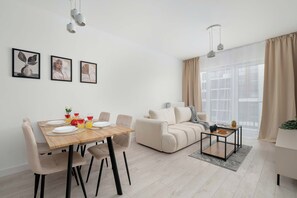 Ein modernes Wohnzimmer mit Essbereich, ausgestattet mit einer Couch, einem Couchtisch und einem Esstisch, der mit Tellern und Gläsern gedeckt ist.
