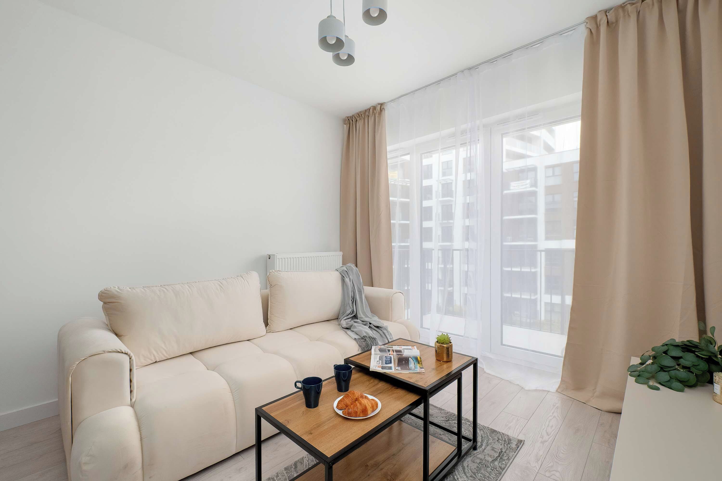 Ein modernes Wohnzimmer mit einem beigen Sofa, einem Couchtisch und einem Fenster mit transparenten Vorhängen.