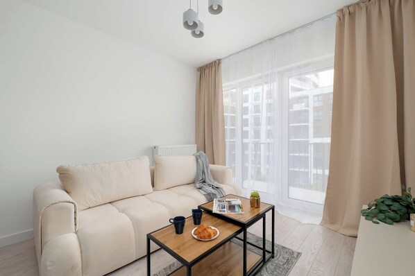 Ein modernes Wohnzimmer mit einem beigen Sofa, einem Couchtisch und einem Fenster mit transparenten Vorhängen.