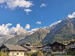 A mountain village with traditional wooden houses, a clear sky, and snow-capped peaks in the background. - New Listing (Les Houches)