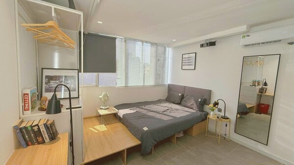 Une chambre à coucher avec un lit, des tables de chevet, un bureau, un miroir et une fenêtre avec des stores.