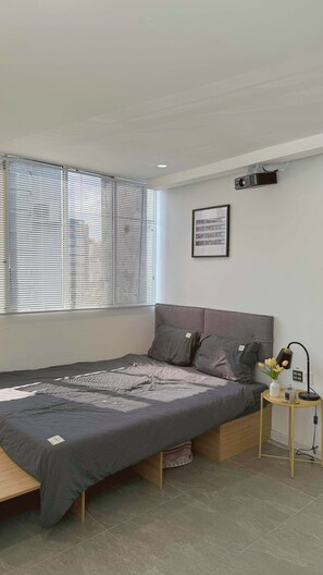 Une chambre à coucher moderne avec un lit, une petite table de chevet, une lampe et une fenêtre avec des stores.