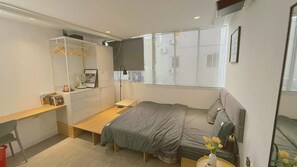 Une chambre à coucher comprenant un lit, un bureau, une armoire et une fenêtre avec des stores.