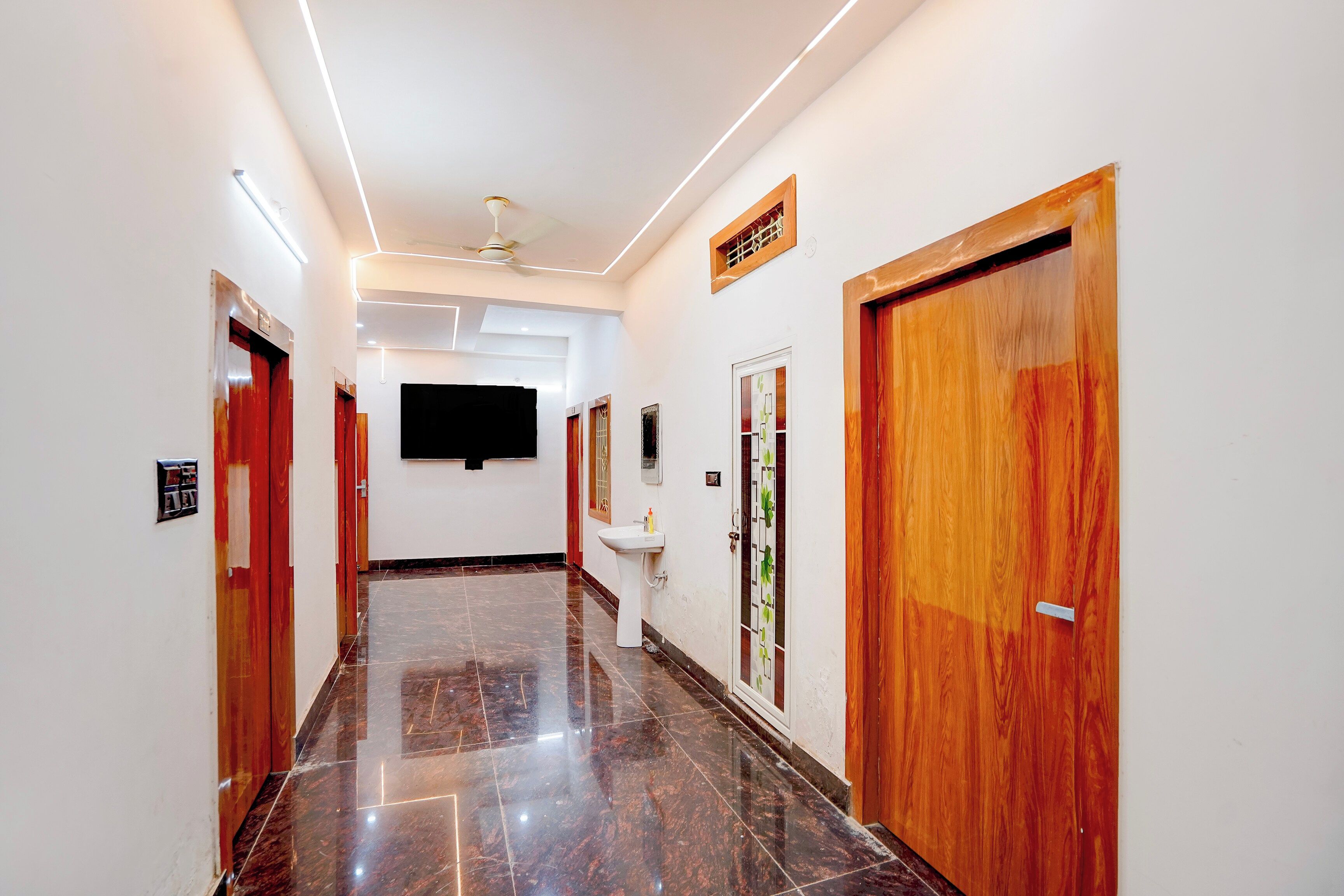 A hallway with a polished marble floor, wooden doors, and a ceiling fan.