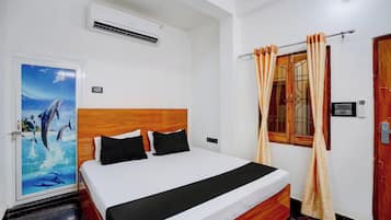 A hotel room with a bed, a wall-mounted air conditioner, a door with a view of the ocean, and a window with curtains.