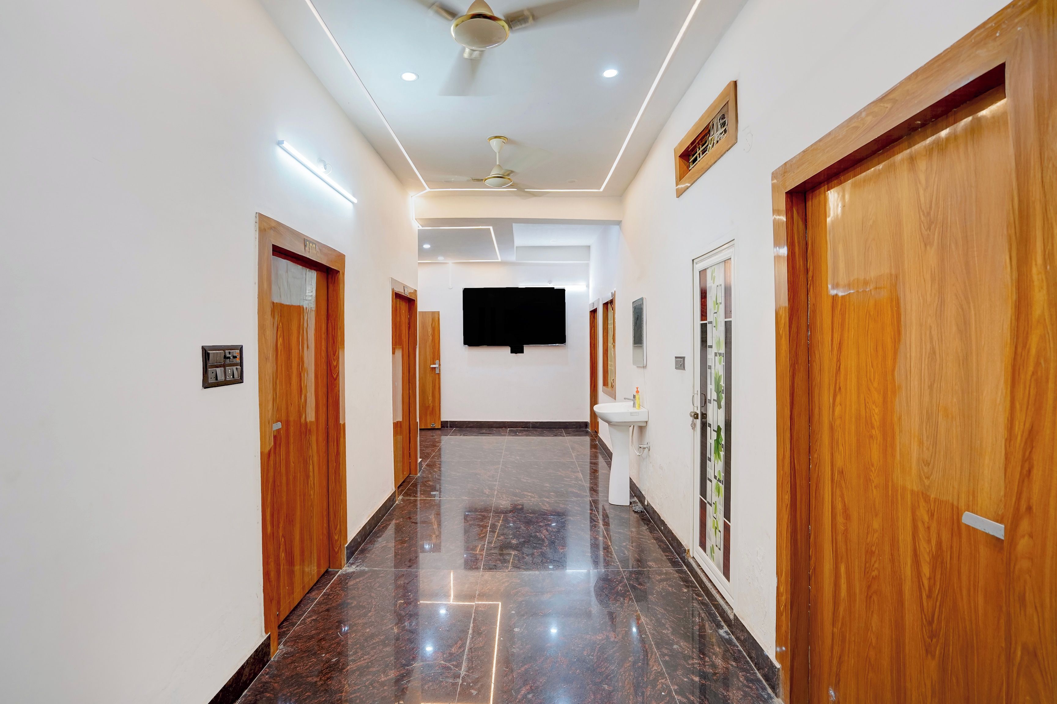 A hallway with wooden doors, a ceiling fan, recessed lighting, a flat-screen TV, and a tiled floor.