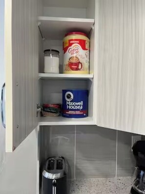 A kitchen cabinet with a coffee maker, a can of coffee, and a Maxwell House coffee filter. - Roku TV, 10 mins to Airport, Charming Suite (Calgary)