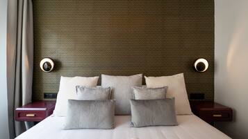 A hotel room with a bed, pillows, a nightstand, and wall sconces.