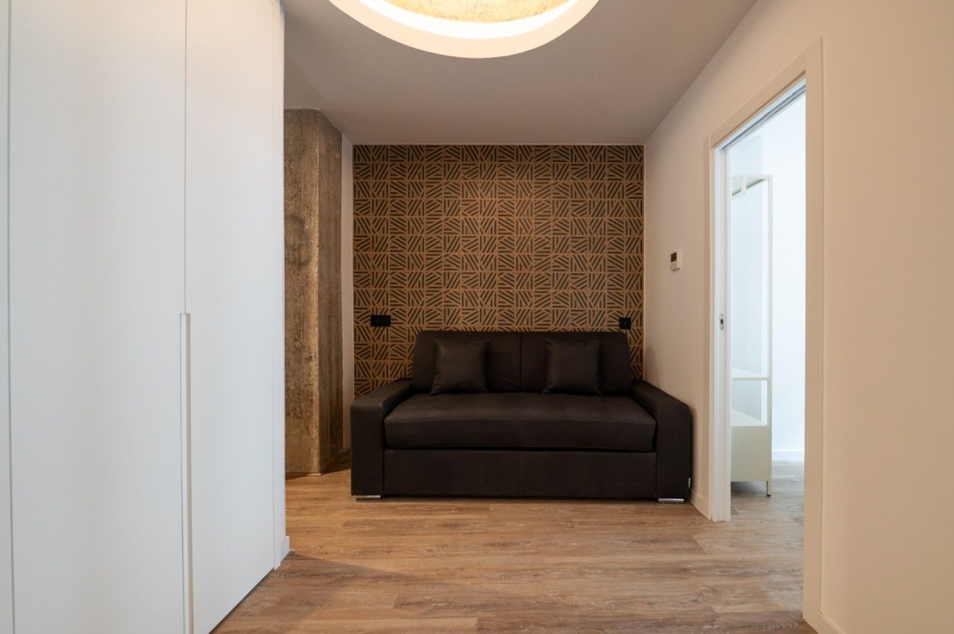 A modern room with a dark sofa, patterned wallpaper, and a wooden floor.