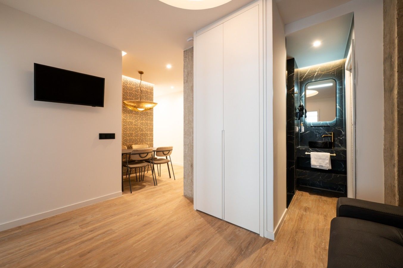 Een modern interieur met een eethoek, een wandtelevisie en een badkamer met een marmeren aanrechtblad en een grote spiegel.