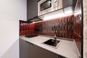 Een moderne keuken met een RVS-spoelbak, een magnetron en een rode achterwand met een patroon.