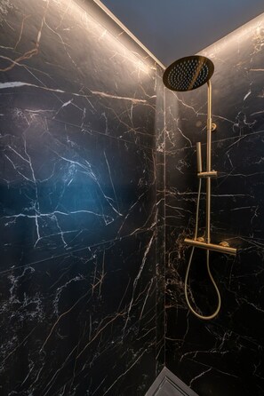 A shower with a handheld showerhead and a handheld rain shower attachment against a dark marble wall with white veining. - A33 Signature Residences - Sol von Monaro * * * * * (Madrid)