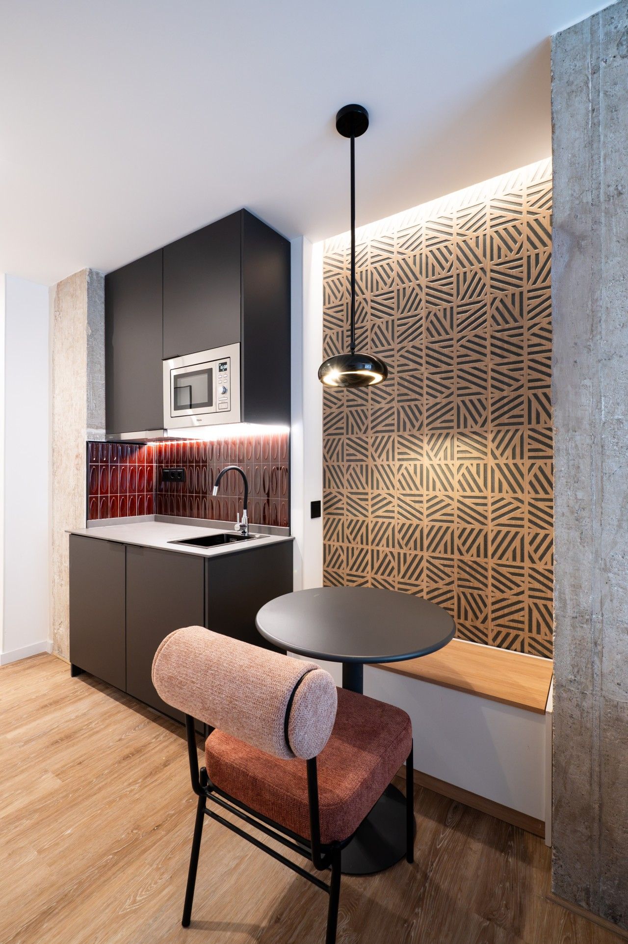 A modern kitchen with a built-in microwave, a round dining table, and a patterned wall.