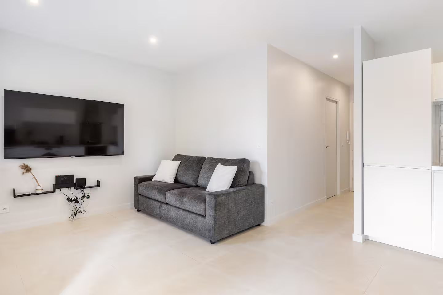 Een moderne woonkamer met een grijze bank, een wandgemonteerde televisie en een minimalistisch interieur.