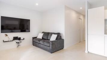 Een moderne woonkamer met een grijze bank, een wandgemonteerde televisie en een minimalistisch interieur.