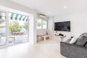 Una sala de estar moderna con un sofá gris, un televisor de pantalla plana montado en la pared y un puerta corrediza de vidrio que da a un patio al aire libre.