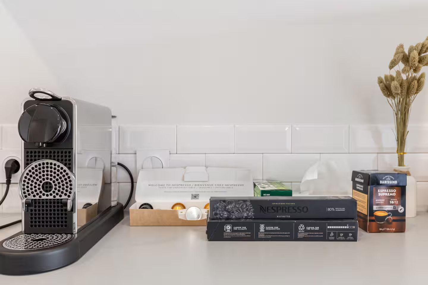 Een Nespresso koffieapparaat, een doos Nespresso capsules, en een barista koffiezetapparaat op een aanrecht.