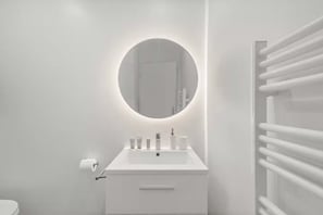 Un baño moderno con lavamanos, espejo y toallero blancos.