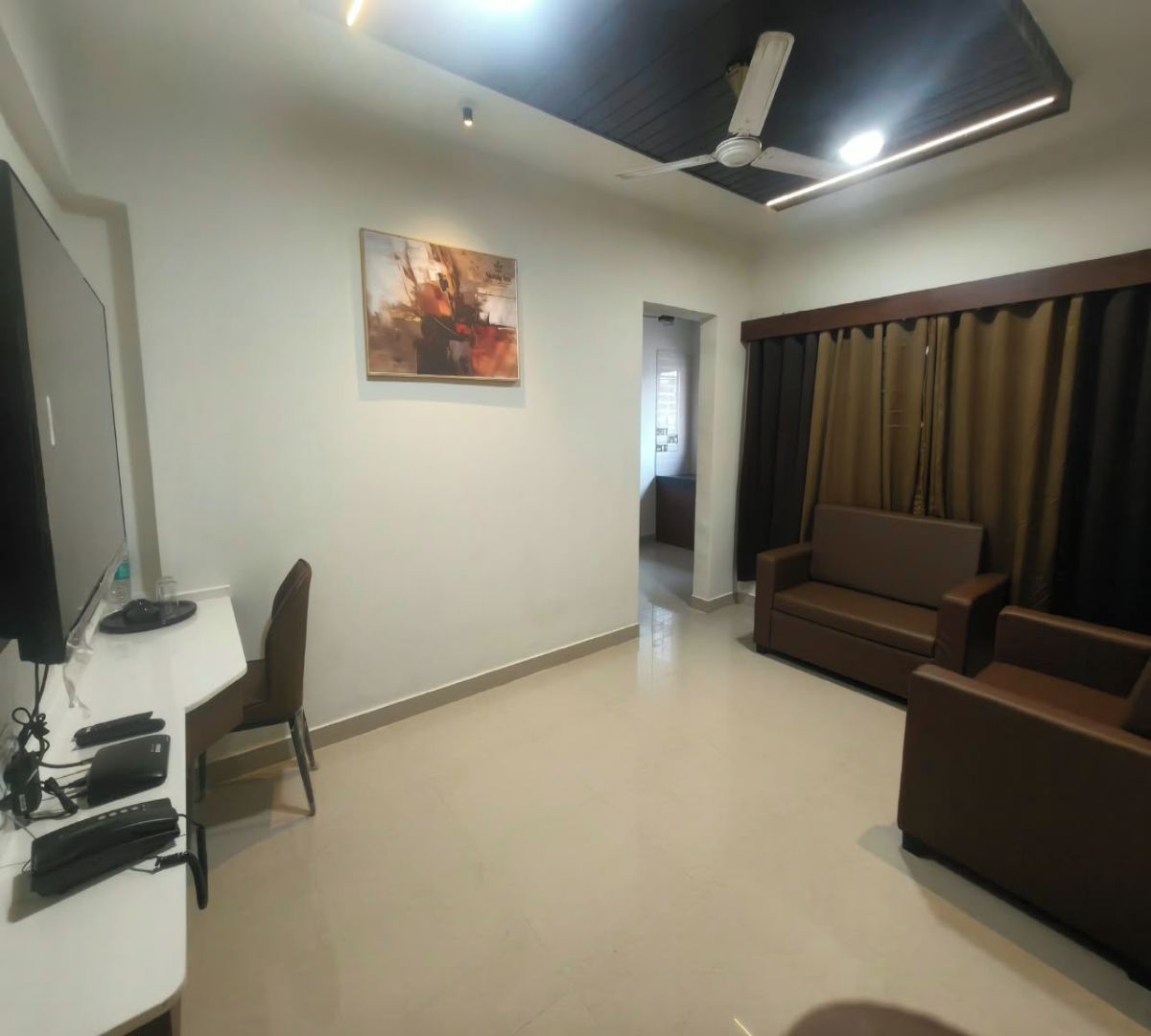 A living room with a flat-screen TV, a sofa, a chair, and a painting on the wall.