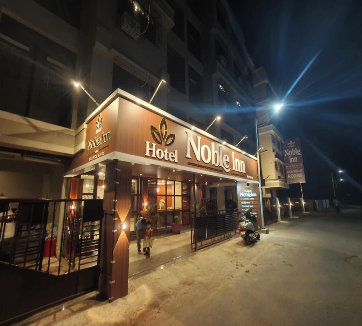 Un hôtel appelé « Noble Inn », avec une enseigne, une entrée fermée par un portail et une moto garée à l’extérieur.