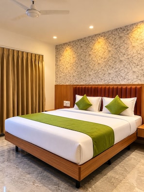 Une chambre d’hôtel avec un grand lit, une tête de lit en bois, des coussins décoratifs verts et un papier peint à motifs floraux.