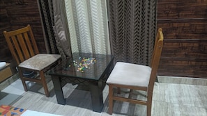 Une table à plateau en verre, ornée d’objets colorés, flanquée de deux chaises en bois dotées d’assises rembourrées.