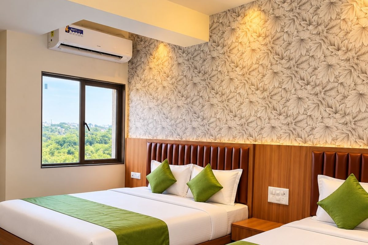 Une chambre d’hôtel avec deux lits, une grande fenêtre, un ventilateur de plafond et un papier peint à motifs floraux.