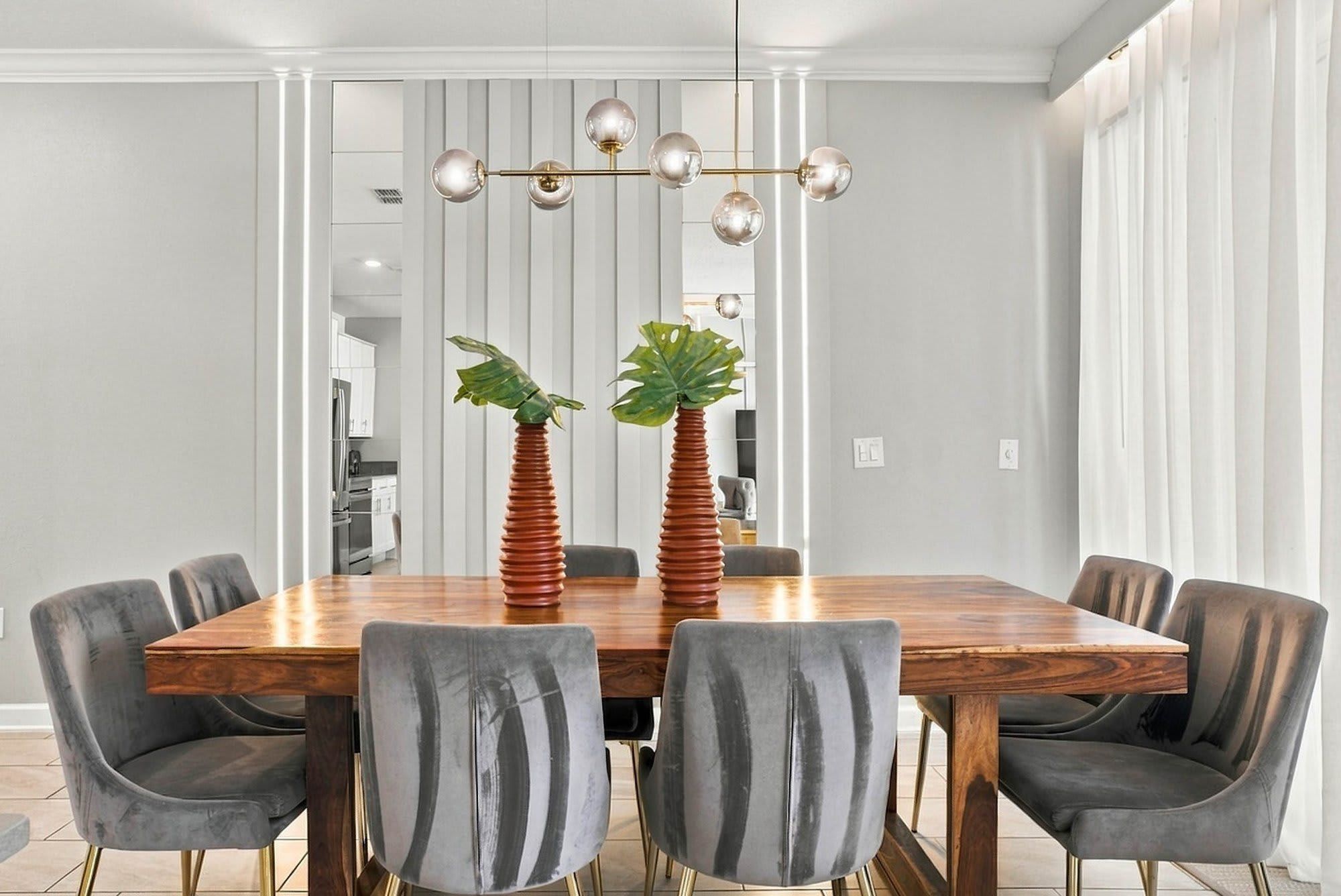Een eetruimte met een houten tafel, zes stoelen en een moderne kroonluchter.