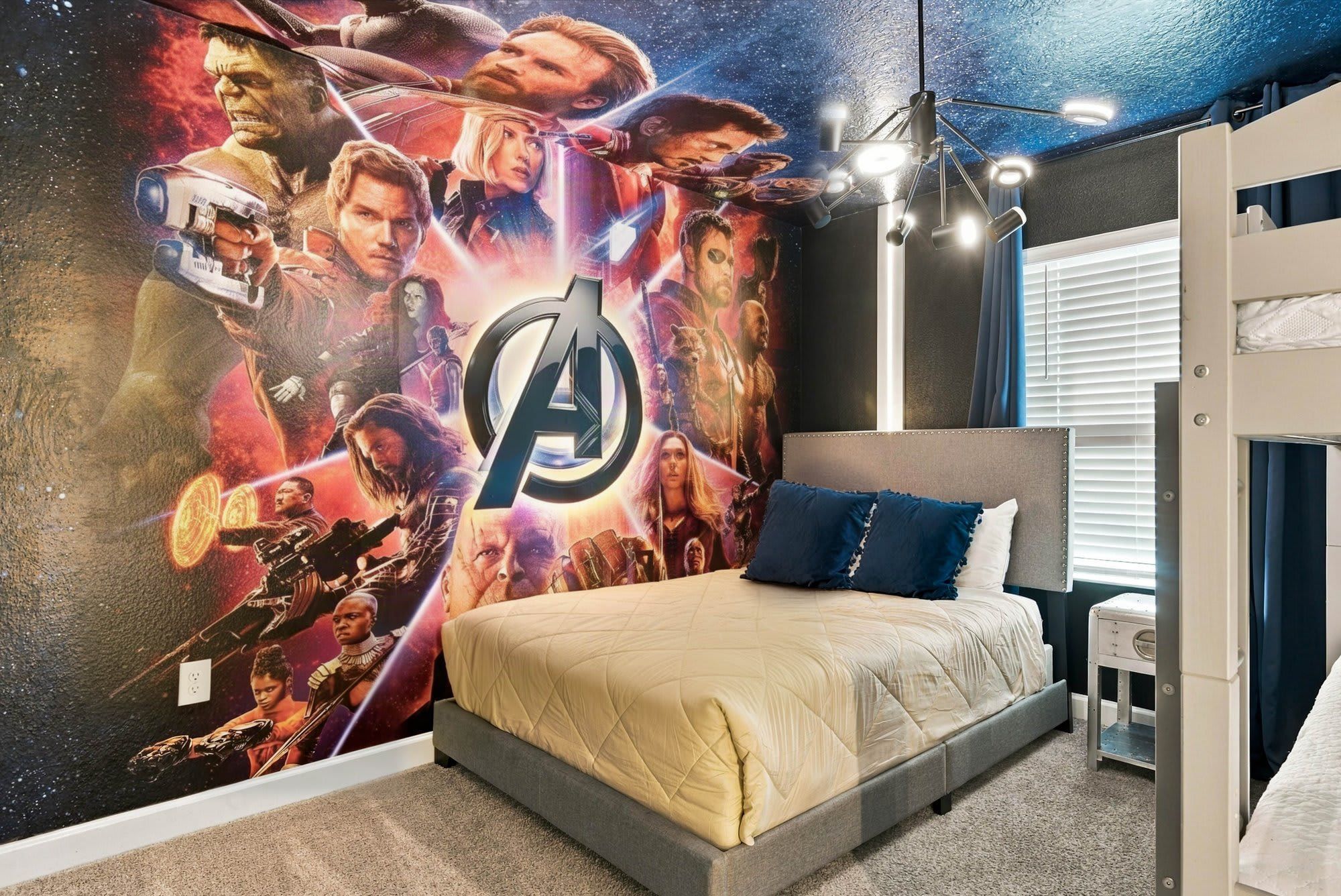 Een slaapkamer met een grote muurschildering, een bed met een grijze hoofdeinde en een nachtkastje.